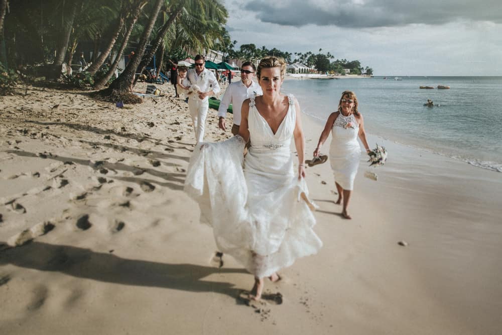 An Intimate Barbados Wedding Mark Caroline Jono Symonds Bride Groom And Members Of The Wedding Party Walking Barefoot Along Beach In Holetown