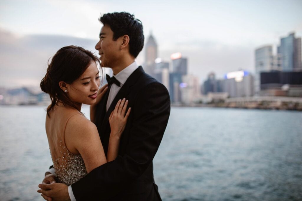 Couple embracing on portrait shoot at Victoria Harbour, Hong Kong with city skyline behind them