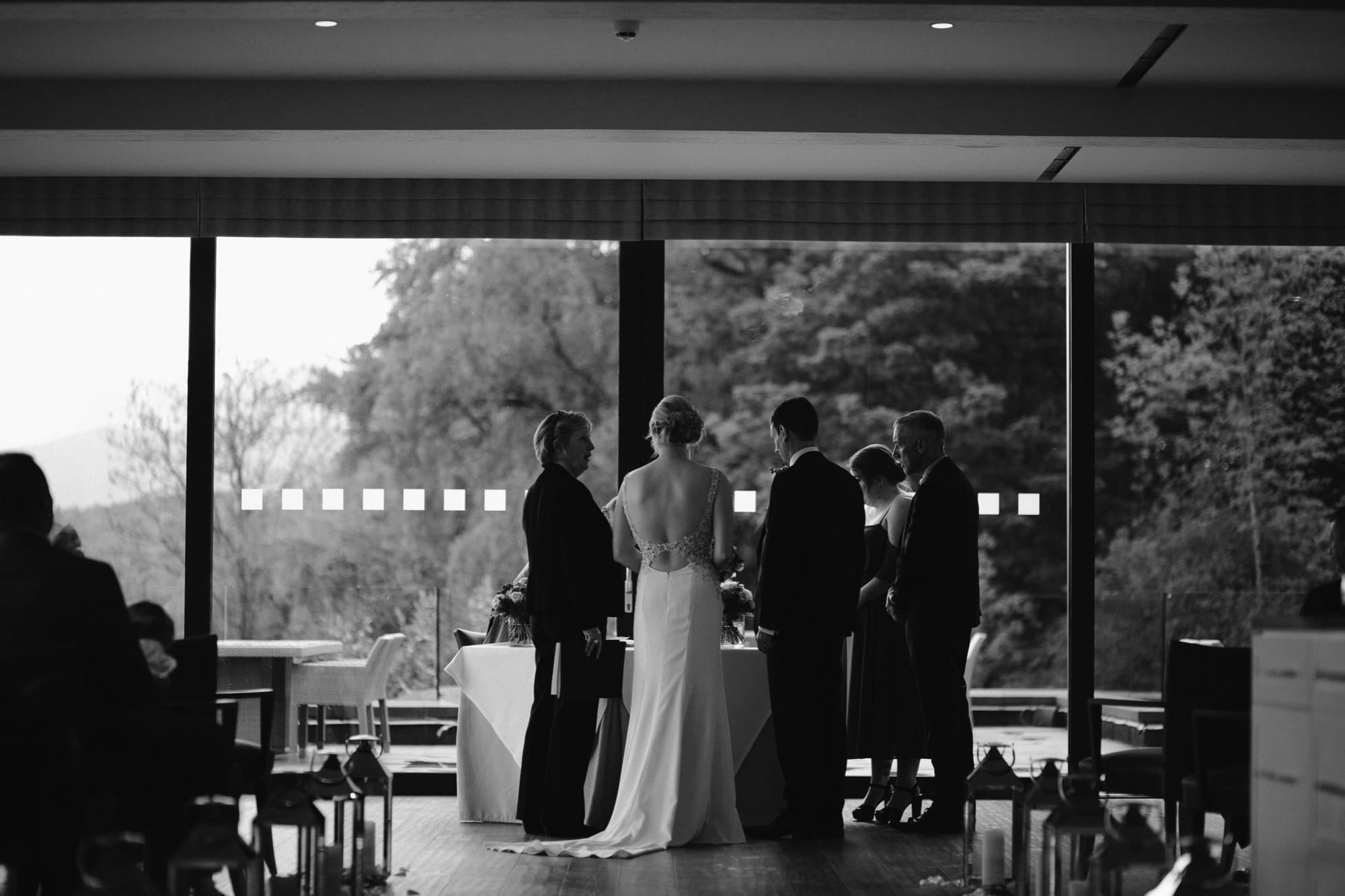 Bride, Groom & Guests stand together near a window at The Samling Hotel in Cumbria, with a table set in the background, capturing the essence of a beautiful wedding gathering.