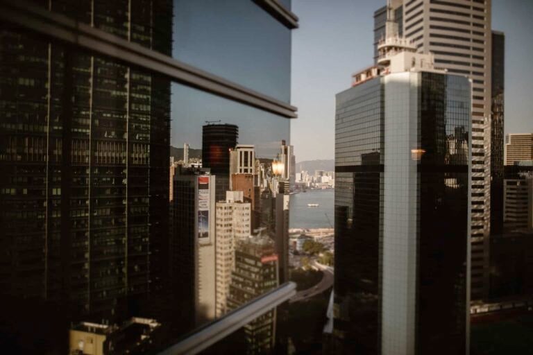 Cityscape with tall modern glass buildings reflecting each other, capturing the elegance of a Hong Kong wedding amidst distant water views and more city structures under a clear sky.