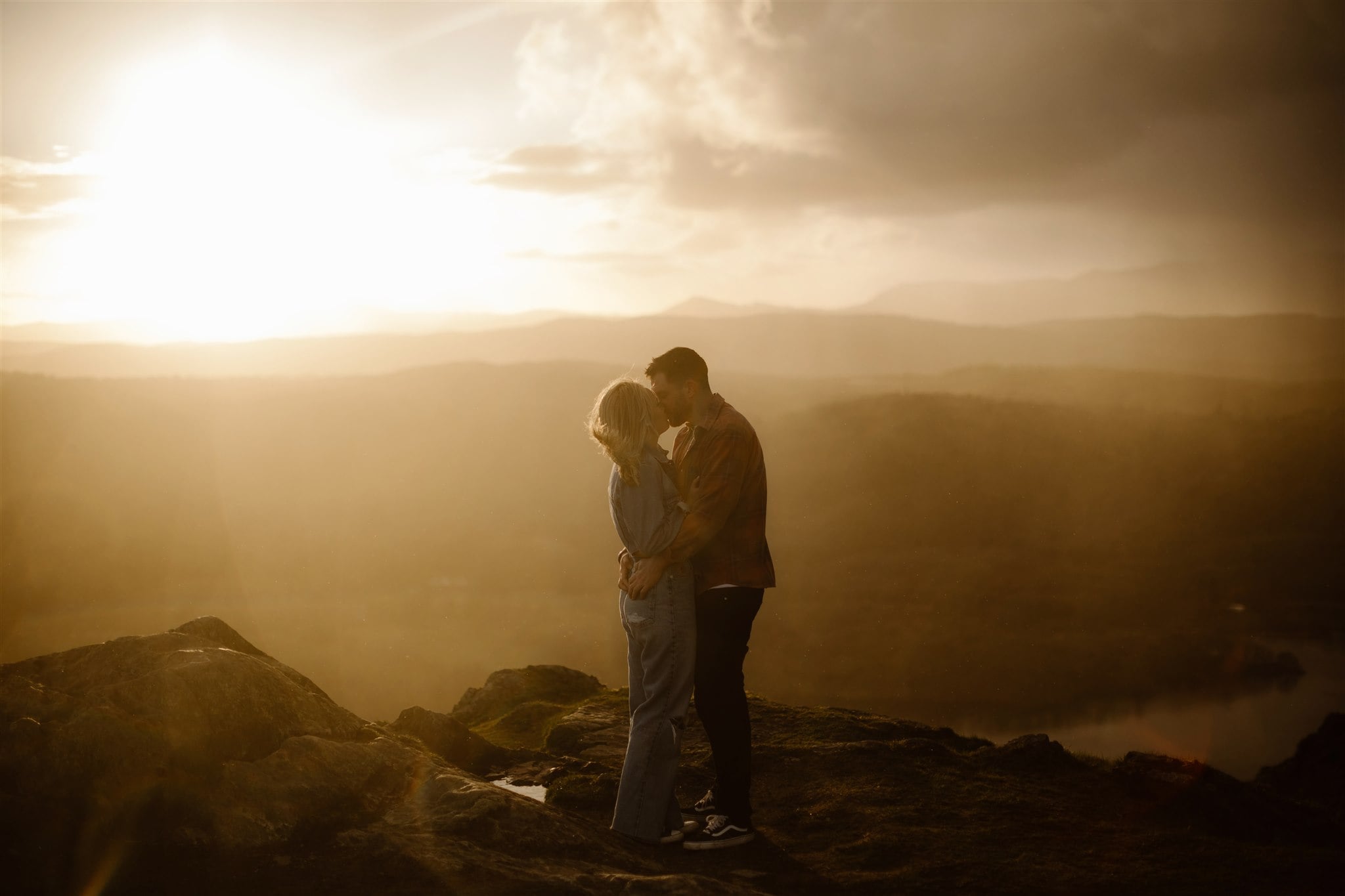 Couple kissing at sunset on top of Lake District Mountain during their engagement shoot