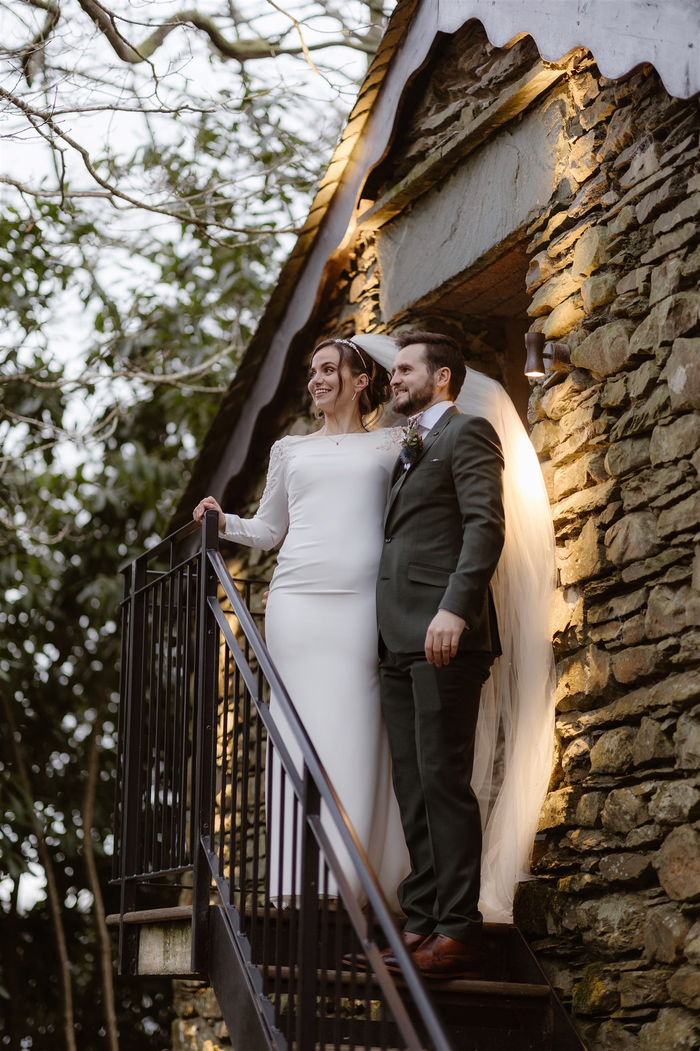 Bride & Groom stoon on steps of the stone boathouse at Town Head Estate