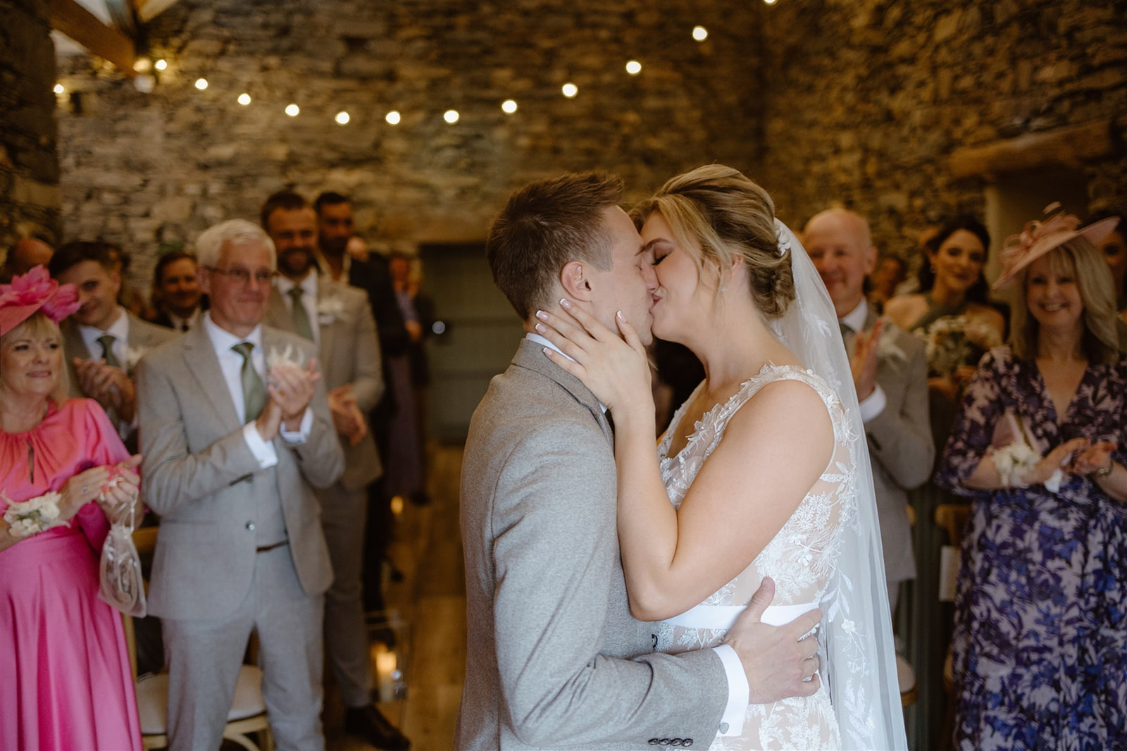 Couple kissing during wedding ceremony in front of guests clapping in The Wedding Barn at Town Head Estate