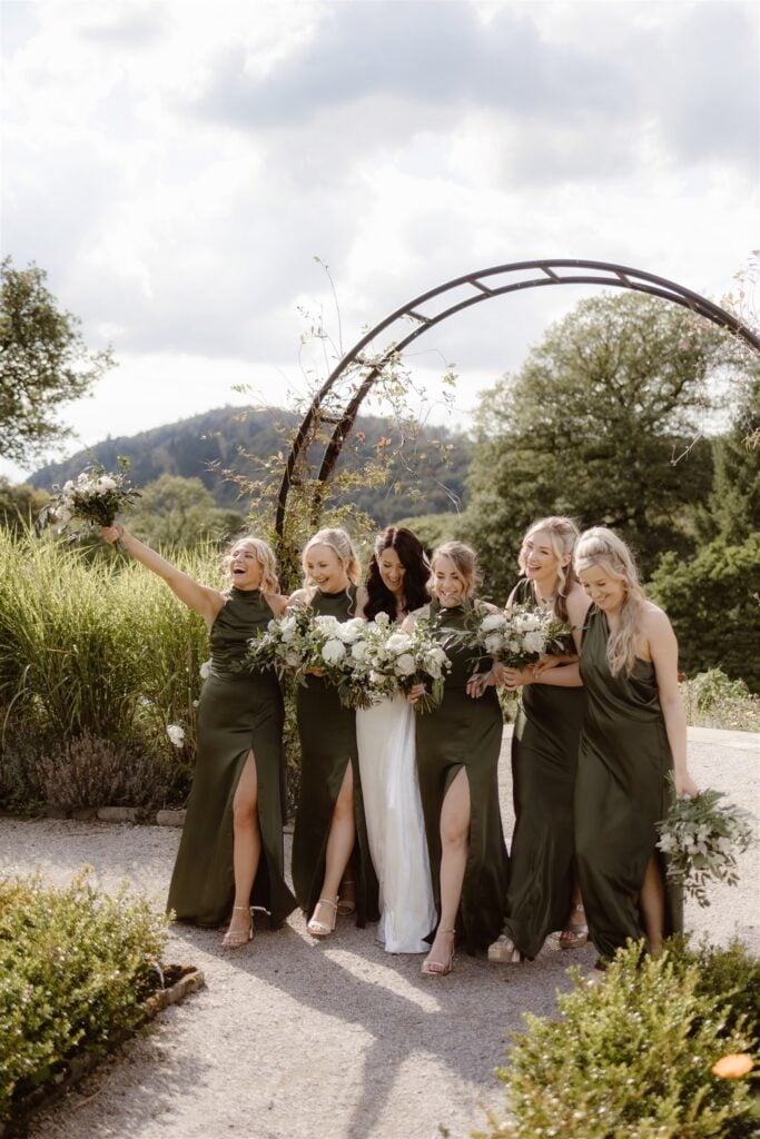 Bridesmaids in green dresses holding bouquets outdoors.