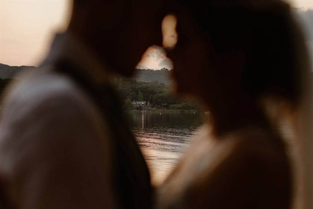 Silhouetted couple by serene lake at sunset.