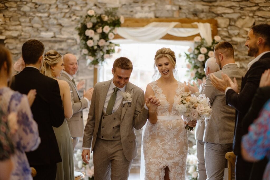 Bride and groom exit ceremony holding hands, guests clap.