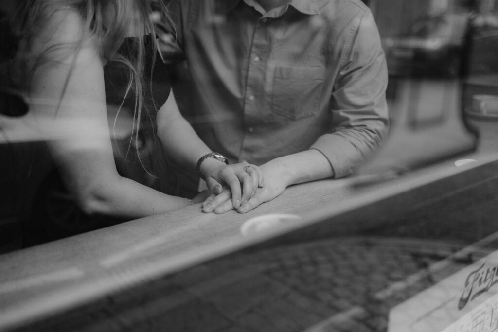 Photographed through a window showing a Woman with her engagement ring placing her hand over her fiancé's.