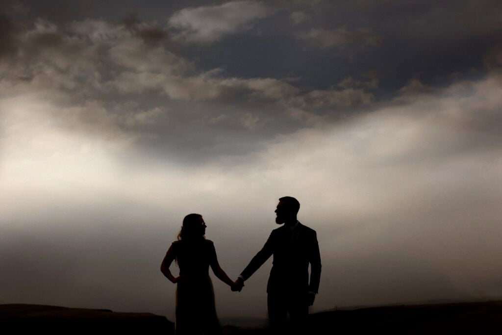 Couple holding hands looking at each silhouetted against sky