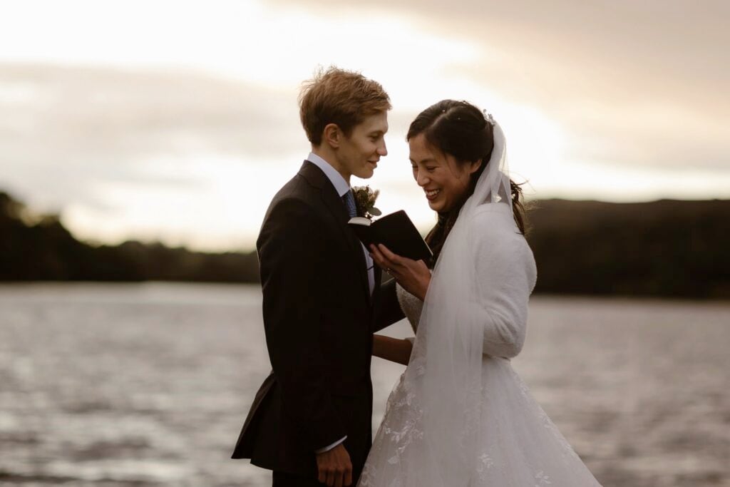 Bride reads vows to her husband by a lake during their elopement ceremony