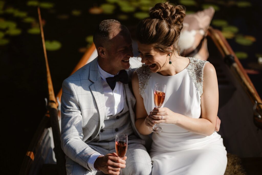 Married couple laughing and drinking champagne in a small rowing boat