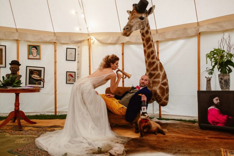 Bride blowing trumpet at her husband in Marquee with a giraffe and other stuffed animals