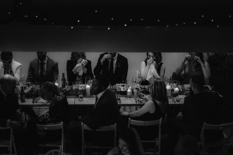 Table of wedding guests shot from above crying during wedding speeches