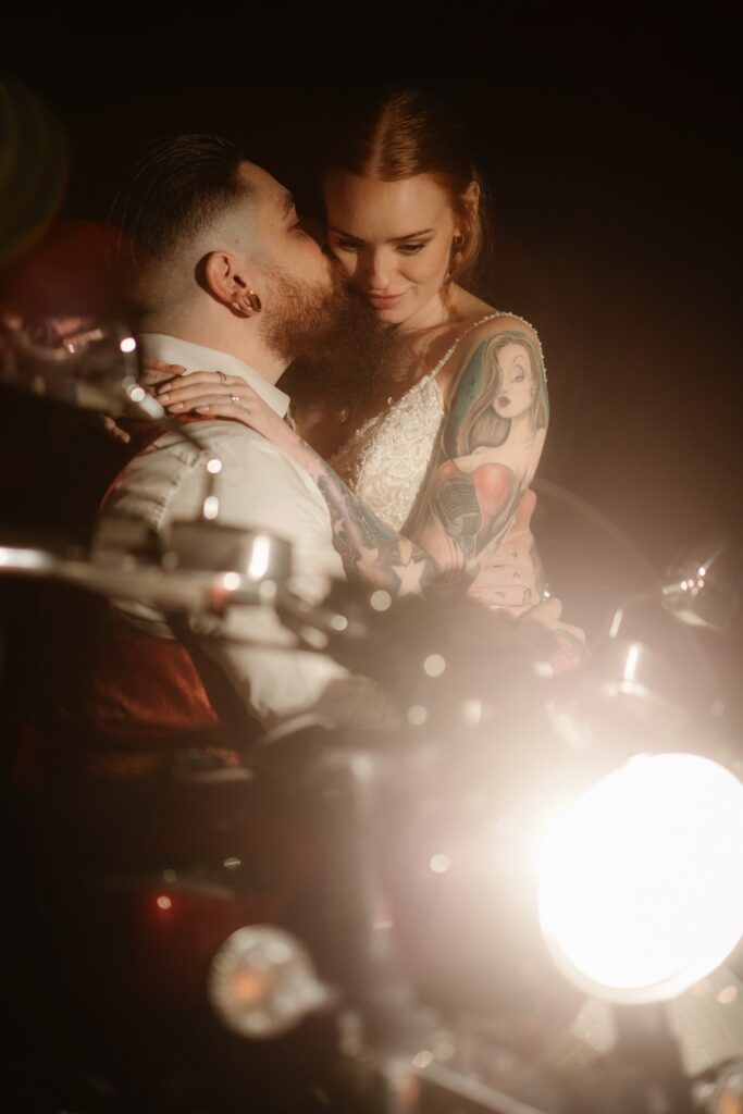Married couple sat by motorbike with light turned on hugging