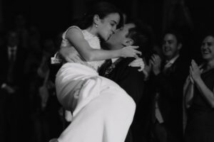 Groom picking up his new wife in his arms and them kissing whilst guests clap.