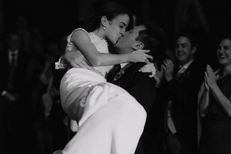 Groom picking up his new wife in his arms and them kissing whilst guests clap