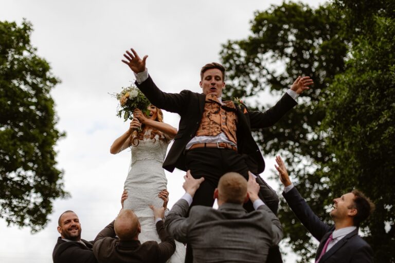 Bride & groom being lifted high into the air by wedding guests