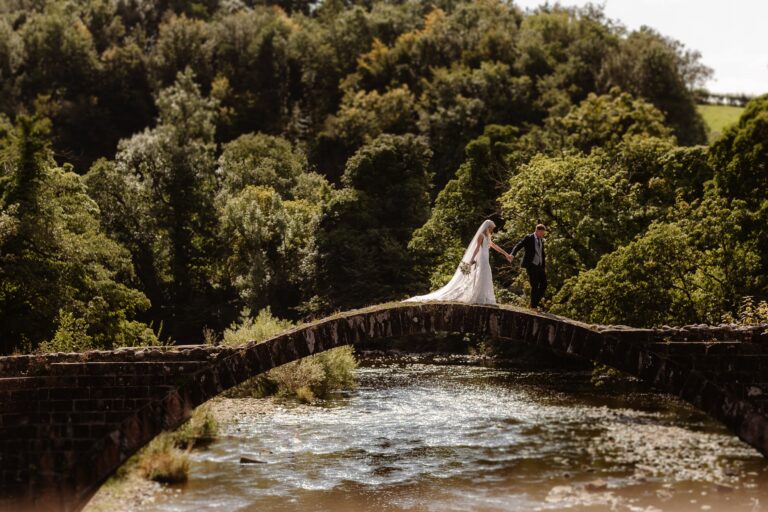 Bride & groom walking over Cromwells Bridge near Mitton Hall