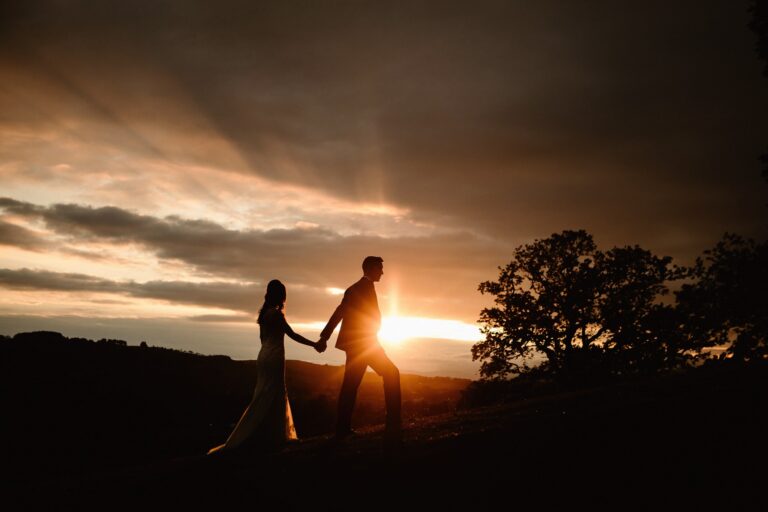 Sunset Silhouette of groom leading bride up a hill by her hand