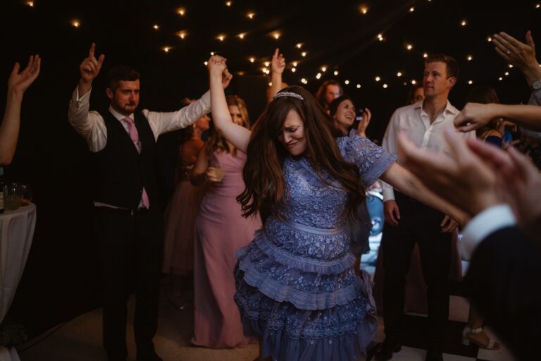 Woman in purple dress dancing in centre of guests throwing arm in the air