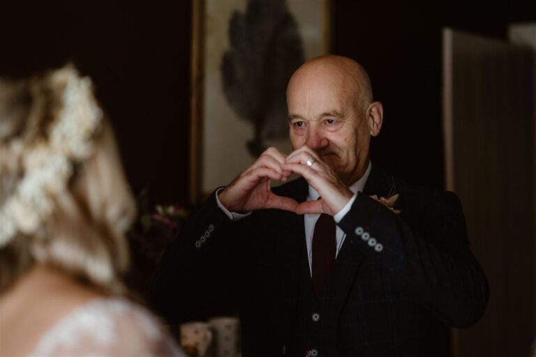 Father of Bride making a heart sign with his hands with tear running down his face as he sees daughter