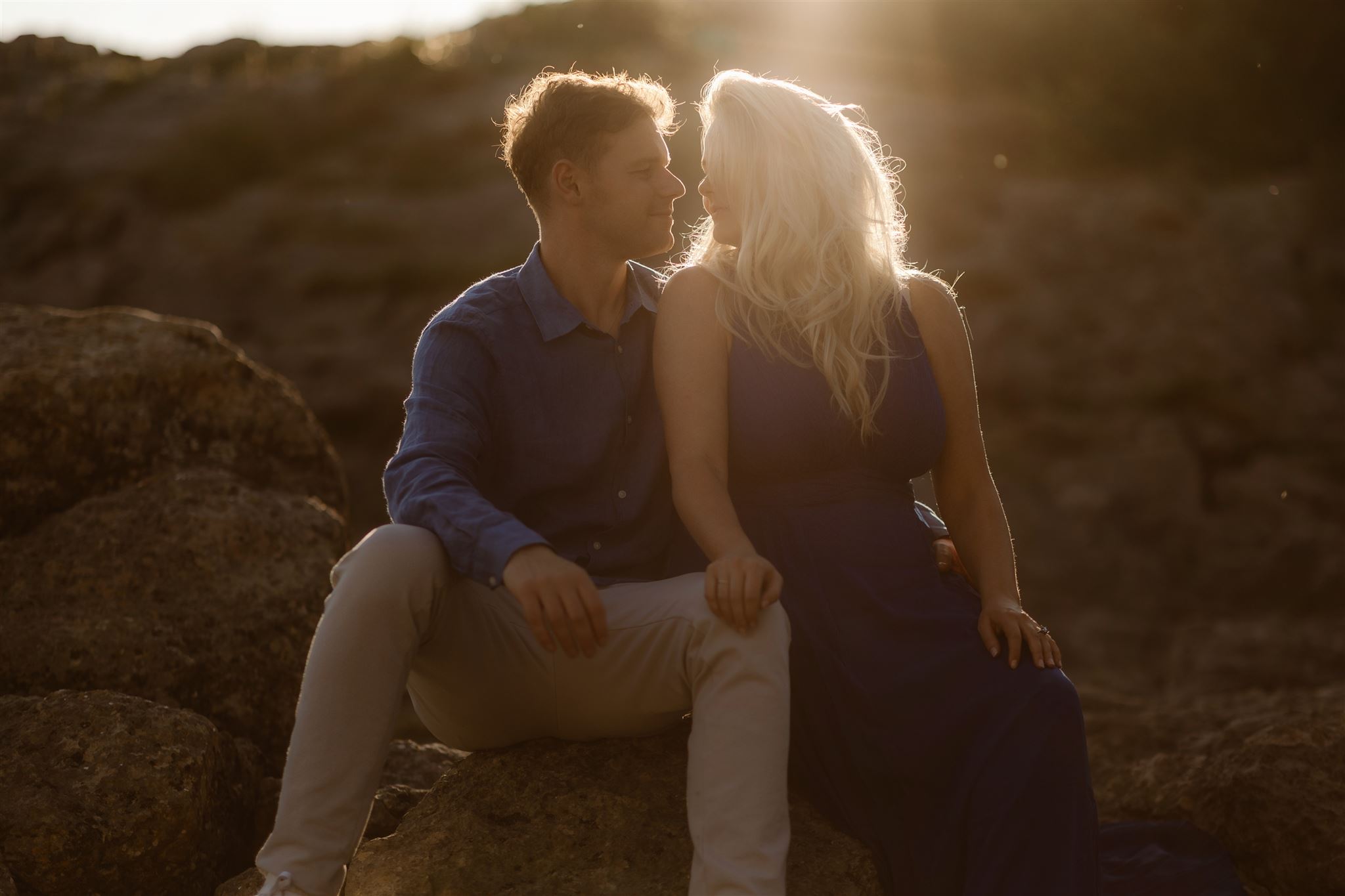 Engaged couple sat on rocks kissing at sunset