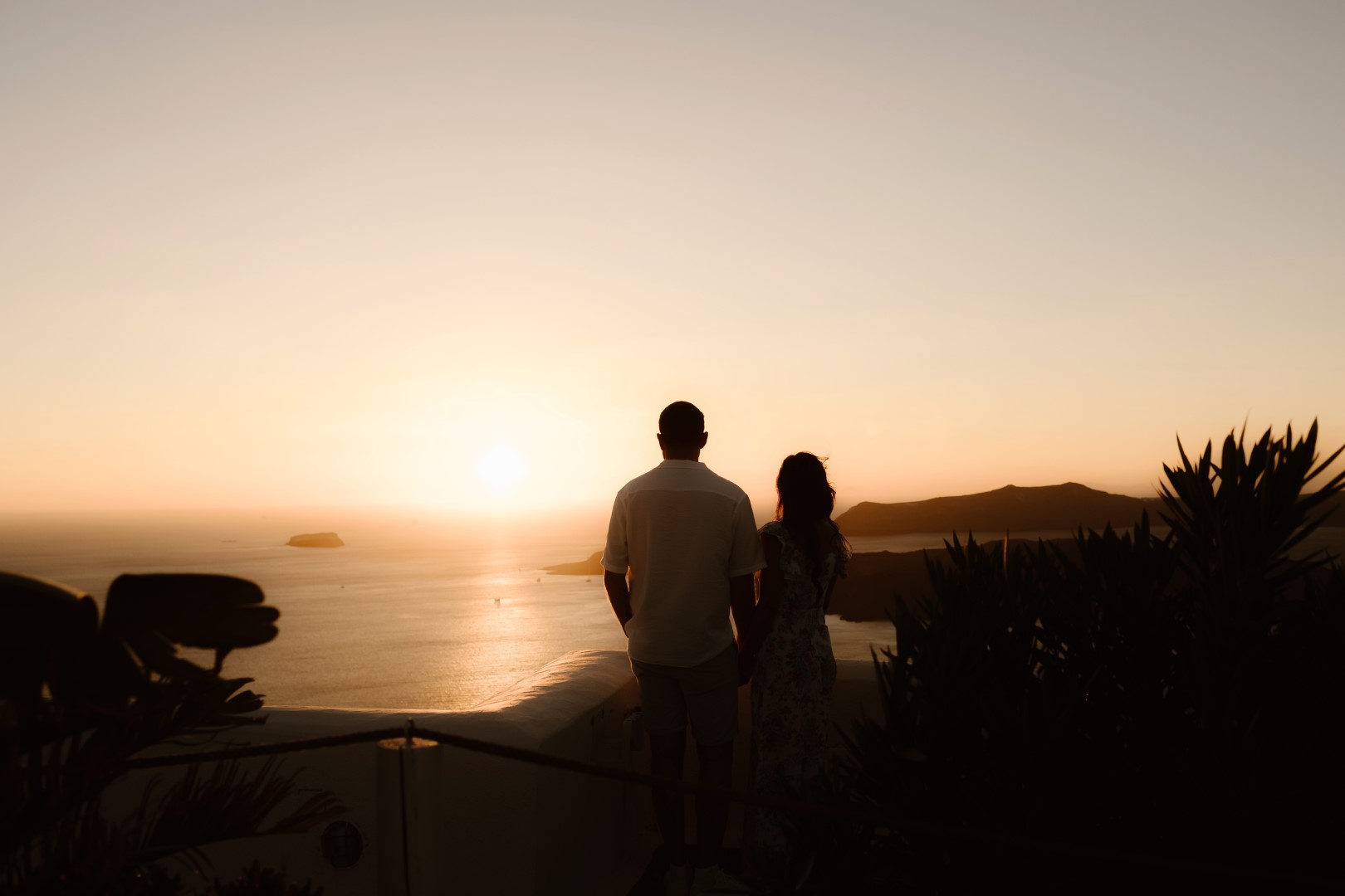 A couple's engagement shoot on a cliff in Santorini, during a sunset overlooking the ocean.
