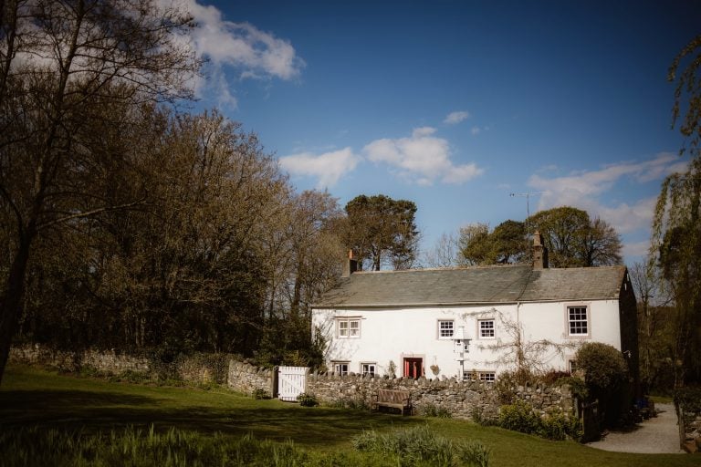Exterior of Low Hall, The Lakes surrounded by trees and blue sky.