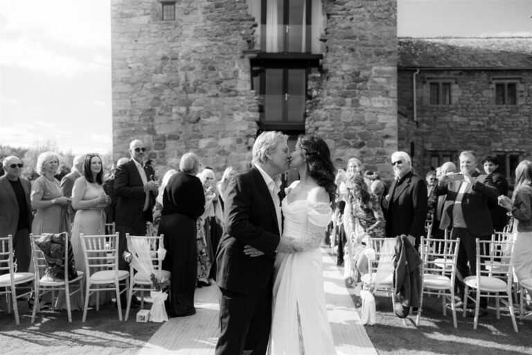 Bride & Groom kiss at the Blencowe Hall outdoor ceremony watched by guests