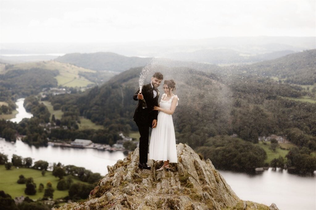 Couple stood on top of mountain spraying champagne