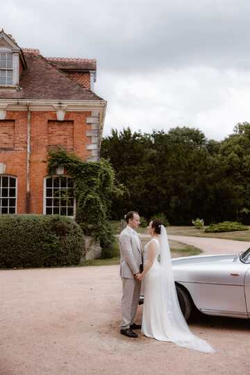 Image of couple stood in front of a red brick building and their wedding car