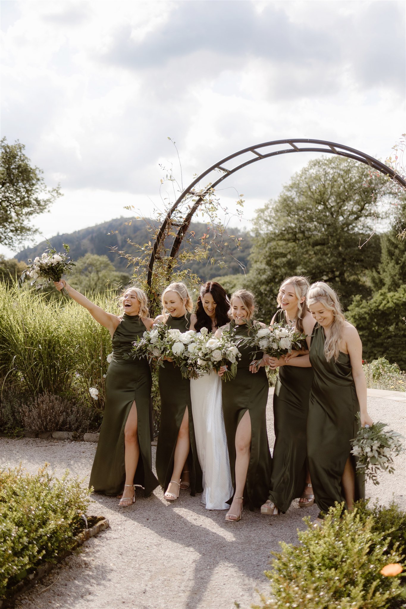 Bridesmaids in green dresses holding bouquets outdoors.