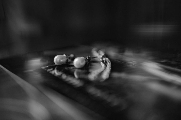 A black and white photo of a pair of pearl stud earrings and a delicate chain bracelet, inspired by the elegance of Appleby Castle, lying on a reflective surface with a soft, blurred background.