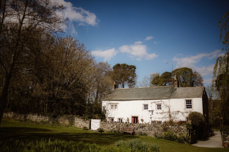 Exterior of Low Hall, The Lakes surrounded by trees and blue sky.