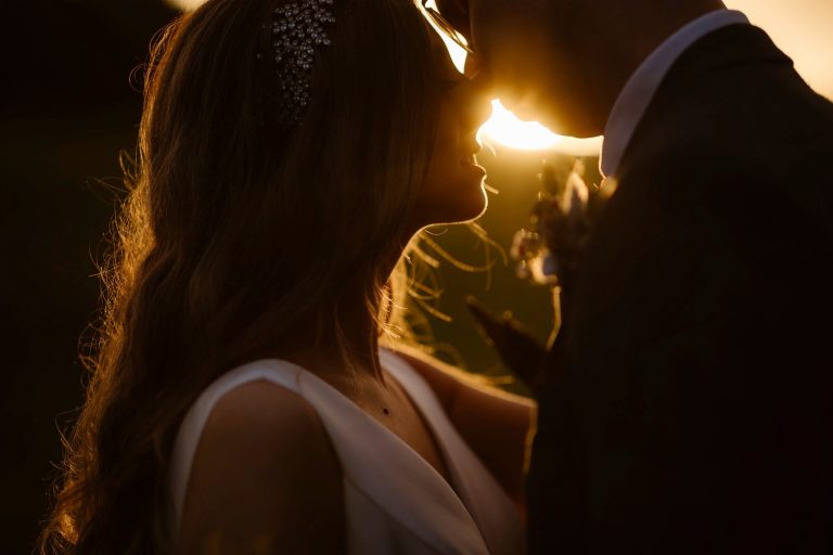 A bride and groom face each other closely at sunset at High Barn & Eden Hall Estate, their faces softly illuminated by the golden light, creating a romantic and intimate atmosphere.